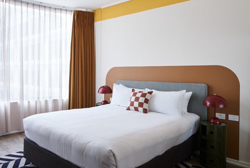 Interior of a hotel room with white bed linen and a red and white chequered cushion, 