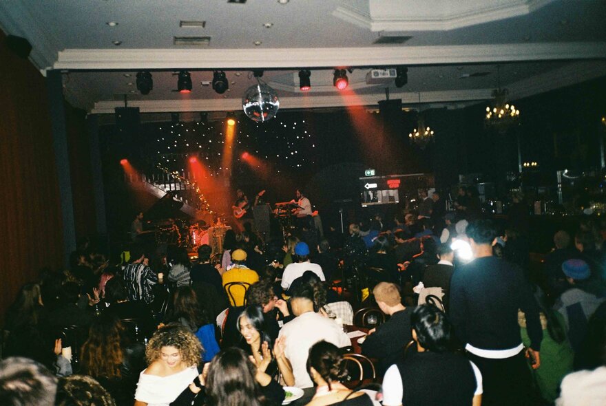 People seated at tables socialising or dancing on a dancefloor at a club.