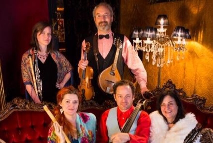 Performers in a bohemian lounge setting with instruments, candelabra and mirrors.
