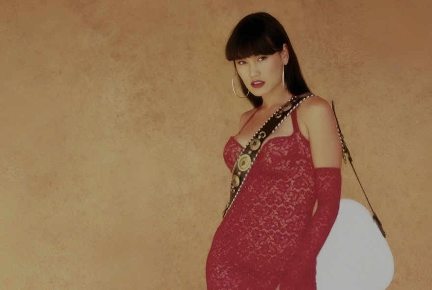 Actress Tia Carrere in the role of Cassandra, from the film Wayne's World, wearing a tight red dress and with an electric guitar slung over her shoulder.