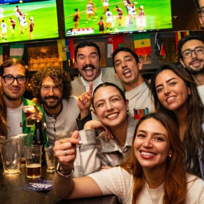 A very happy group of people in a bar posing for a photo with sport on the TVs in the background.