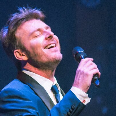 Singer Craig Martin wearing a suit and singing into a microphone.