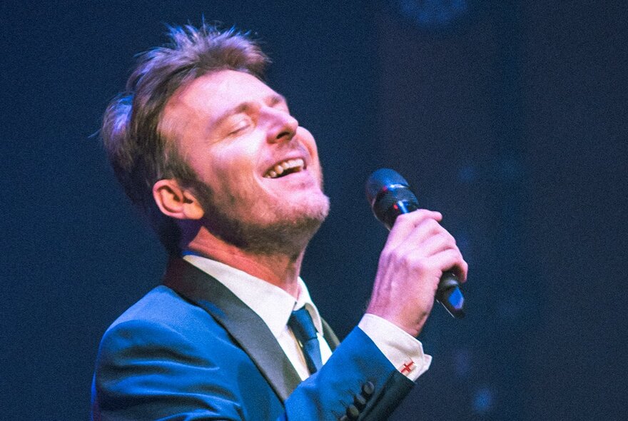 Singer Craig Martin wearing a suit and singing into a microphone.