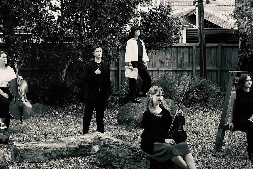 The Changing Wilds Ensemble posed outdoors in a suburban backyard, some with their instruments, in black-and-white.