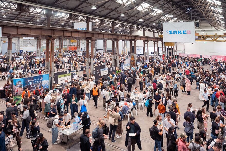 Large crowds of people walking around a hall that is hosting a food and drink expo.