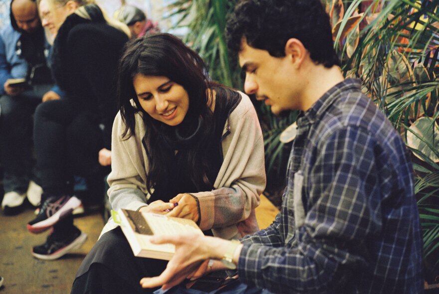 Two people thumbing through a book in an outdoor garden space. 