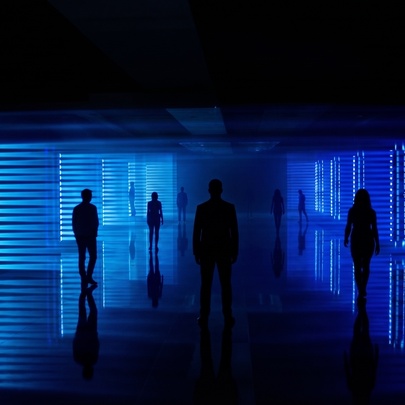 A light show experience with people walking through a darkened space with a deep blue light illuminating them.
