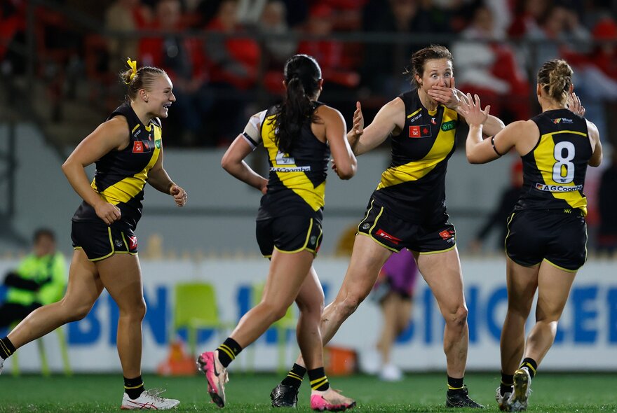Four members of the Richmond AFLW team running around on the footy field. 