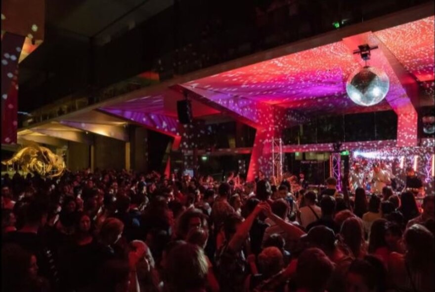 Patrons dancing at a nightclub with a pink and purple-lit stage and disco ball.