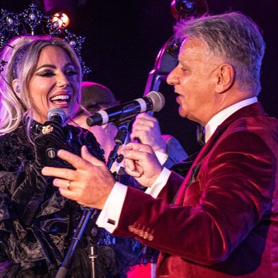 A male and female singer, each holding a microphone, performing on a stage.