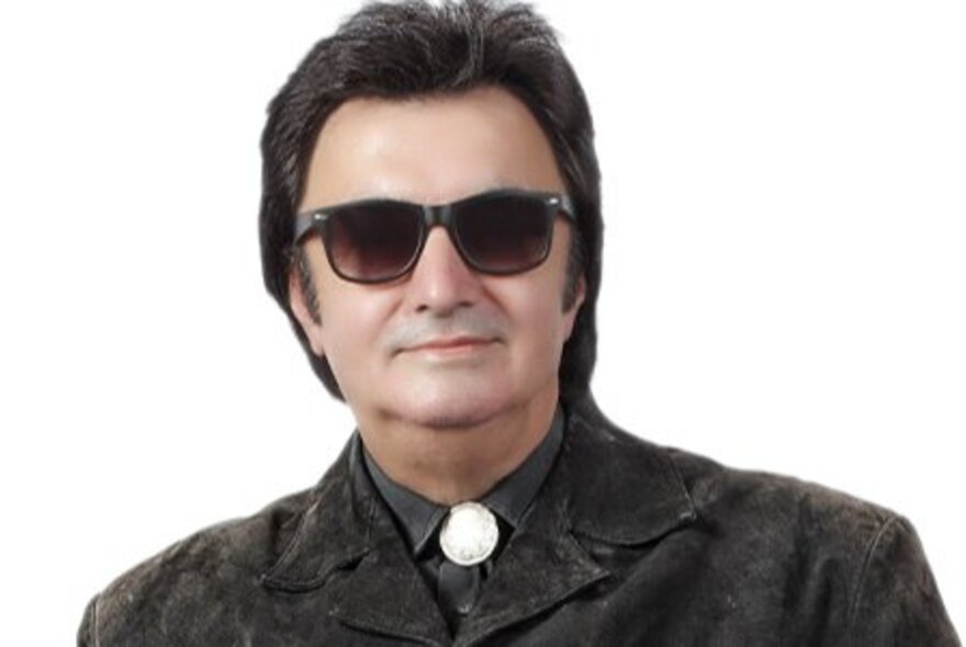 Musician dressed like Roy Orbison with dark glasses, Western shirt and dark hair.