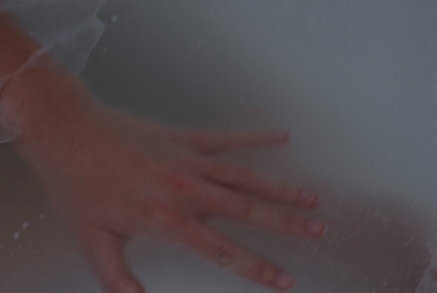 A blurred, mysterious photo of a person's hand with fingers splayed. 