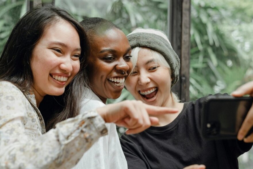 Three young adults smiling with their heads close together.