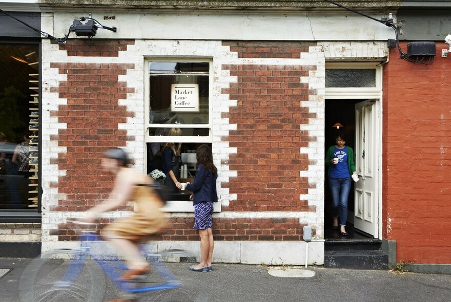 Person ordering coffee at window of a small coffee shop in a red and white brick building.