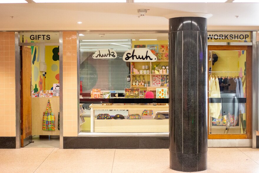 The exterior of a shop called shuh. with a large black column out the front. 