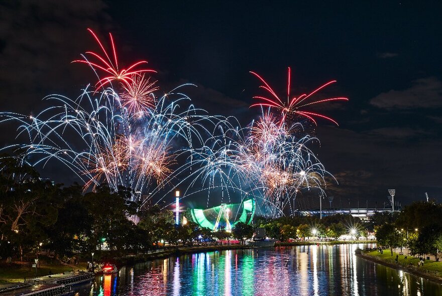 Nighttime fireworks display on the banks of Melbourne's Yarra River, with MCG in the background.