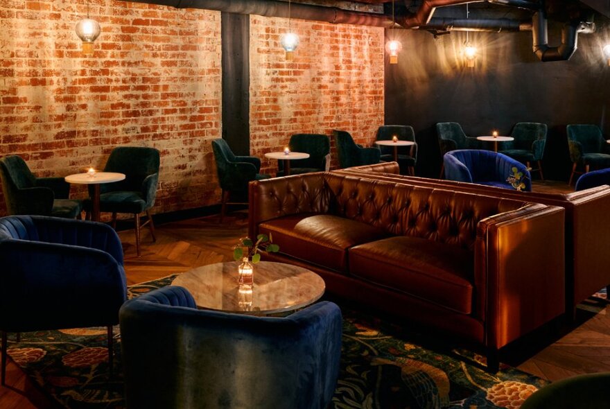 Moodily lit cocktail area with lounge and club chair seating, red brick wall and tables.