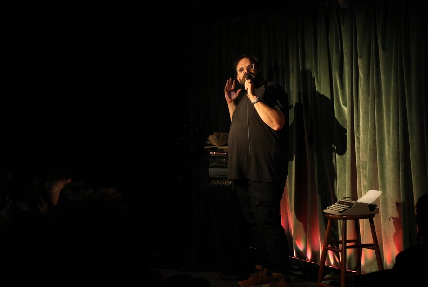 A person spotlit on a stage performing, in front of green curtains.