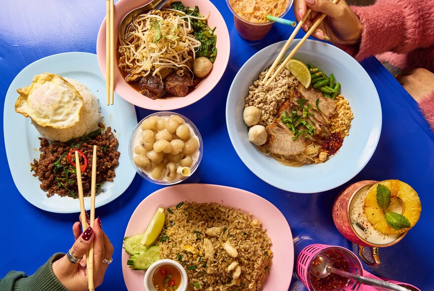 Four Thai dishes and drinks on a blue table.