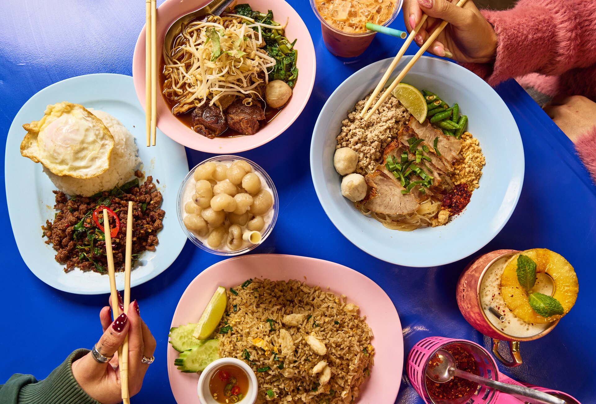 Four Thai dishes and drinks on a blue table.