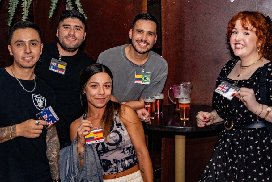 Five people in a bar setting smiling and holding up small cards with flags on them.