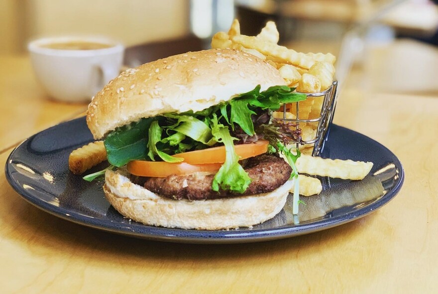 A hamburger with a basket of crinkle-cut fries on a plate.