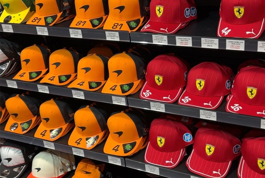 F1 branded racing caps in different team colours, on display on shelves in a shop.