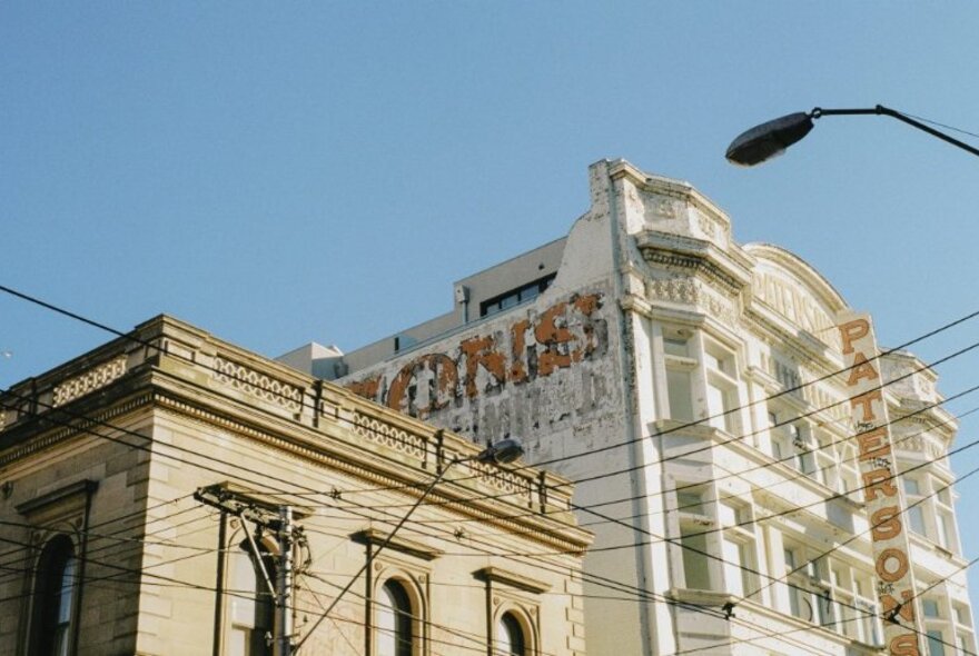 Looking up at the top of ornate older buildings in a streetscape, the old advertising sign decayed but still visible on the side. 