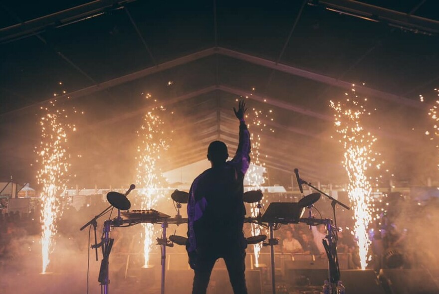 Back view of a musician and musical equipment silhouetted on a stage facing the audience with sparkling lighting effects.