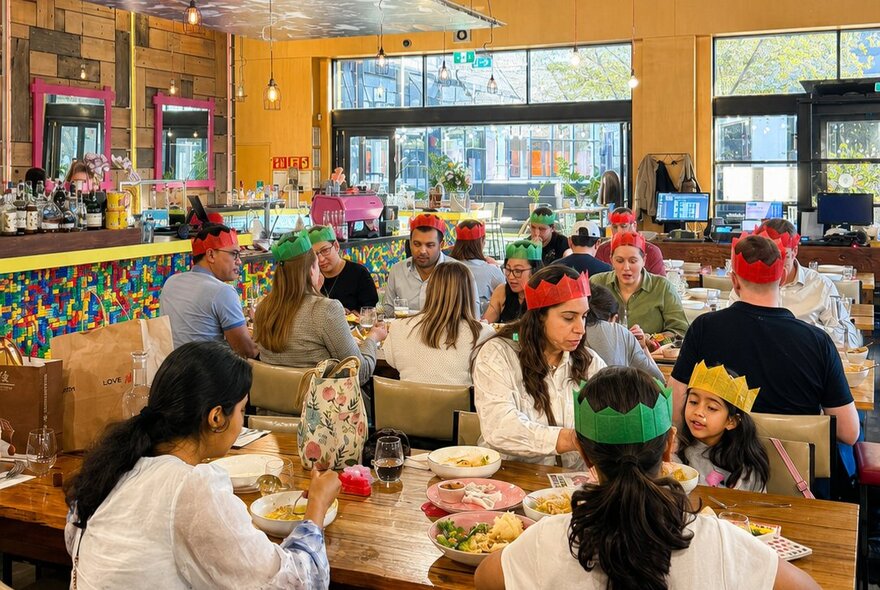 Customers wearing party hats, dining at tables in an indoor venue.