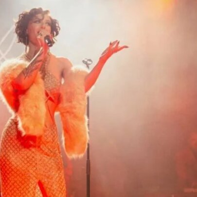 Singer wearing orange strapless gown and wrap singing into a microphone in a smoky club.