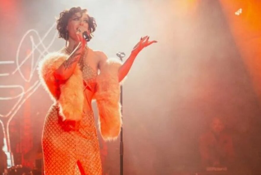 Singer wearing orange strapless gown and wrap singing into a microphone in a smoky club.