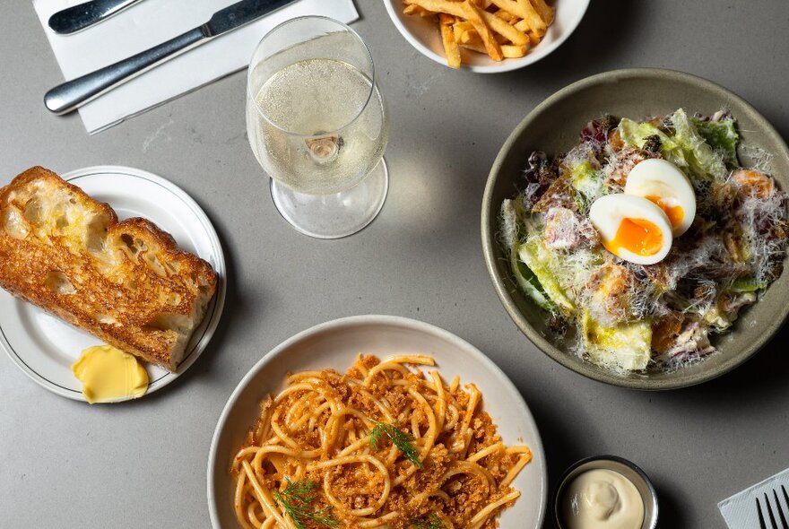 Looking down on a table with spaghetti, Caesar salad and toast with a glass of wine.