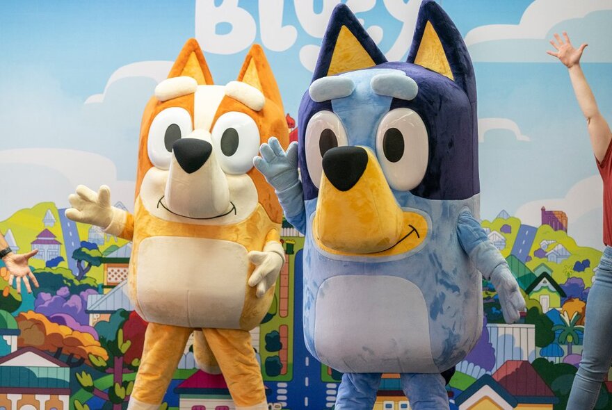 Life size animated dog characters Bluey and Bingo live on stage in an interactive theatre show, with a painted backdrop.