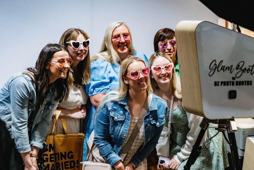 Group of women wearing denim jackets and sunglasses smiling into a camera.