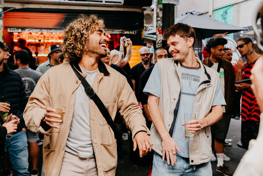 Two men holding drinks, dancing in a crowded bar.