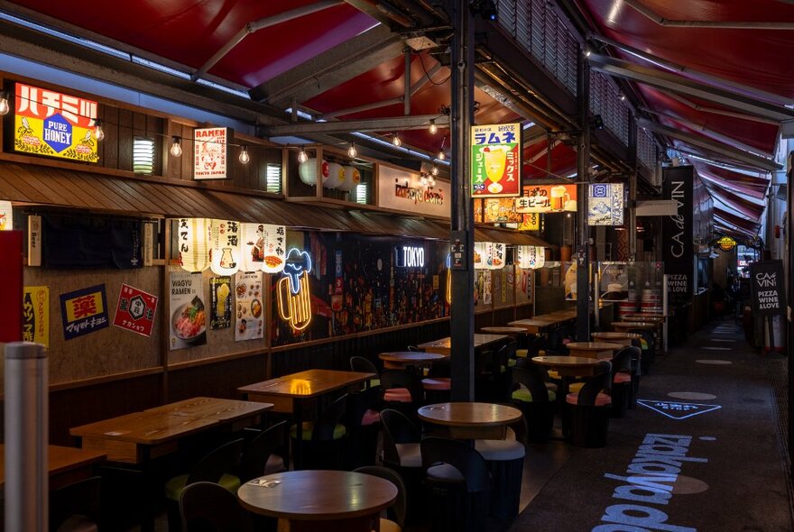 Japanese bar with lots of tables and chairs and illuminated signs for lighting.