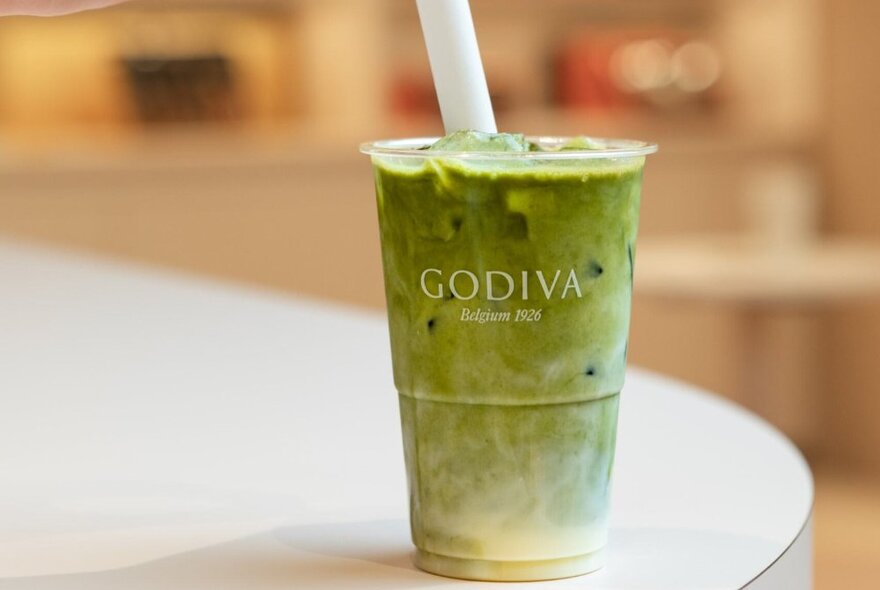 A matcha and white chocolate drink in a clear plastic takeaway cup, with the letting GODIVA printed on the front.