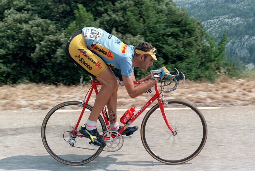 A professional cyclist bent low over his red race bicycle riding on a road.