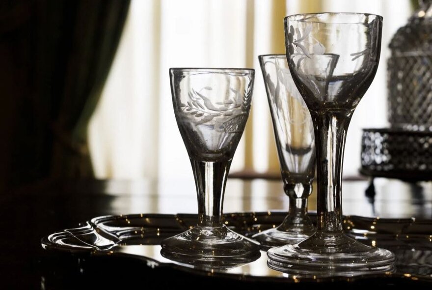 Lead crystal glasses glowing on a table with light streaming in through curtains.