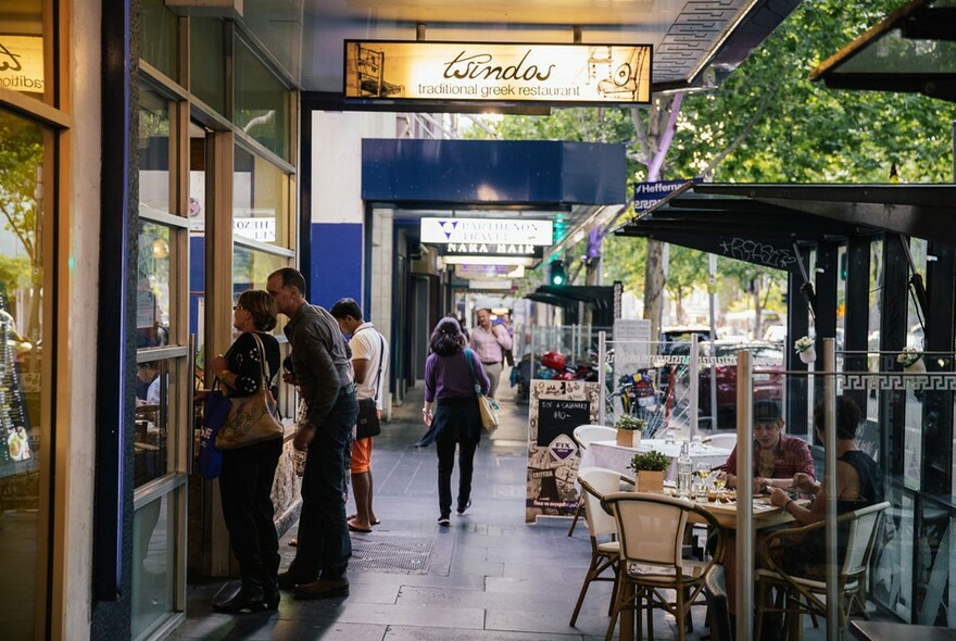 Tsindos exterior with people scanning the menu beside outdoor tables.