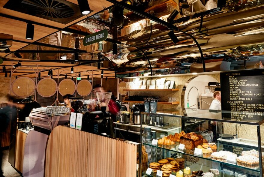 A cafe counter with cakes and pastries and a barista preparing coffee.