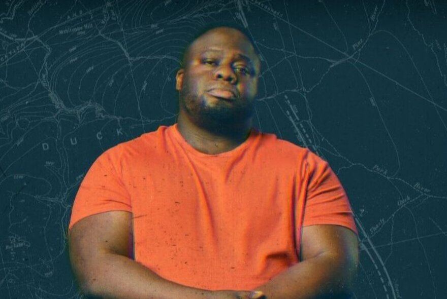 Comedian Nabil Abdulrashid wearing an orange t-shirt, arms folded in front of his chest staring straight ahead.