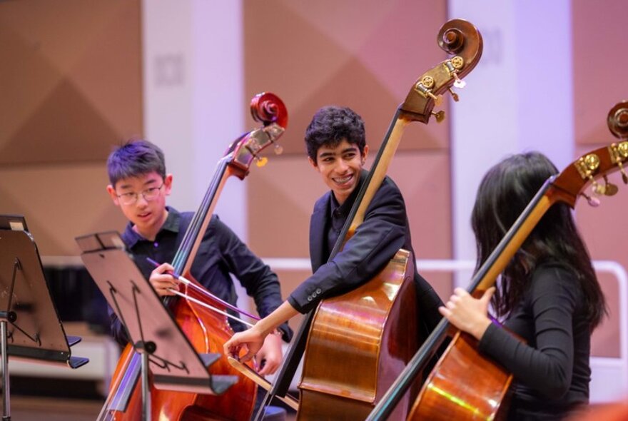 Three young double bass musicians dressed in black, on stage.