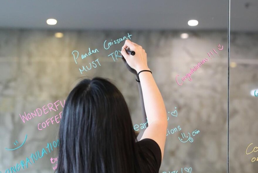 A woman writing menu items on a glass window of a cafe with a paint pen.