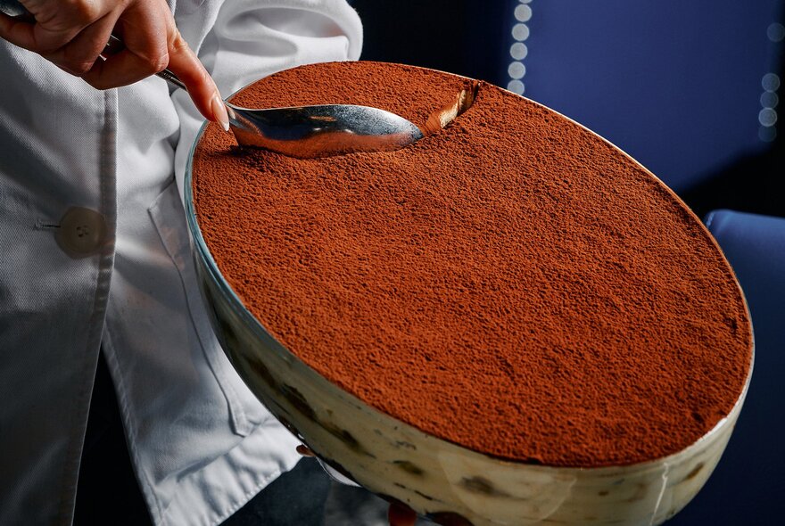 A chef taking a scoop out of a large bowl of tiramisu.