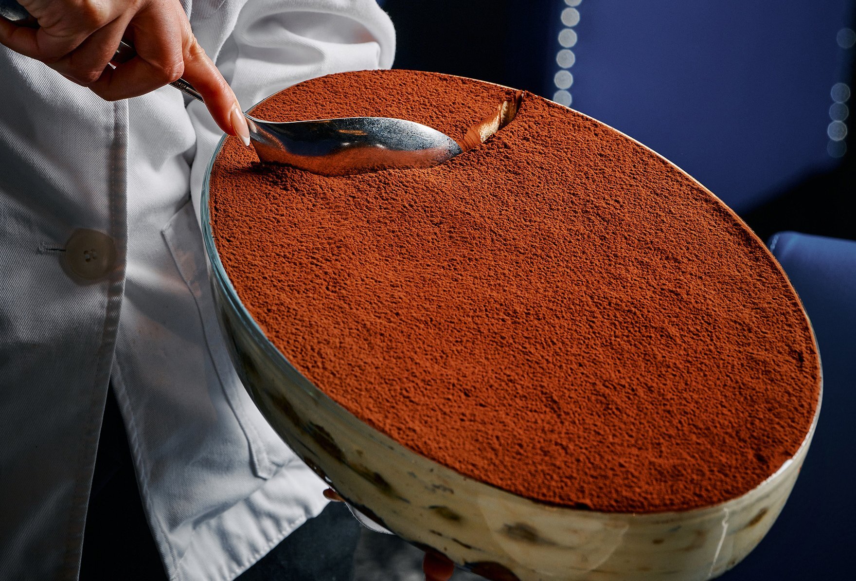 A chef taking a scoop out of a large bowl of tiramisu.