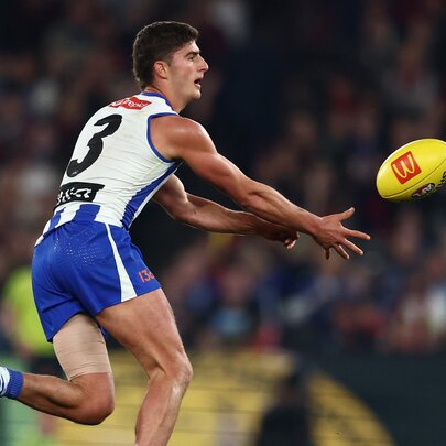 A North Melbourne AFL player handballing a yellow football during a match.