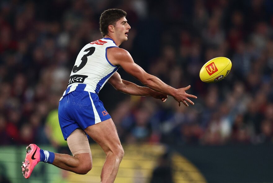 A North Melbourne AFL player handballing a yellow football during a match.
