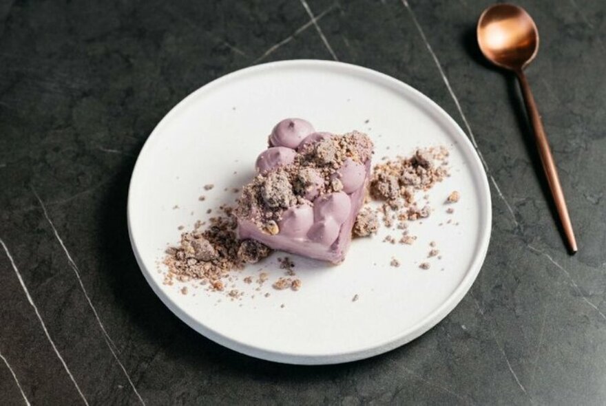 A pink meringue dessert with crumbs and a copper spoon